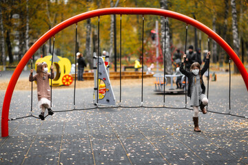 children in the playground in masks, girls friends play through the net in the park, protection from the virus, social distance and friendship, quarantine and restrictions