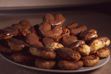 Palmier biscuits covered of chocolate on a plate. Heart-shaped puff pastry, pig's ear, palm leaves cookies, elephant ears, french hearts, shoe-soles.