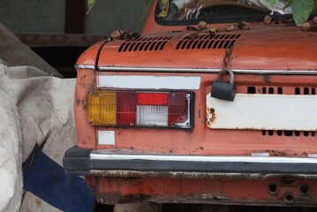 one old colored taillight on a red rusty car by a gray iron bumper