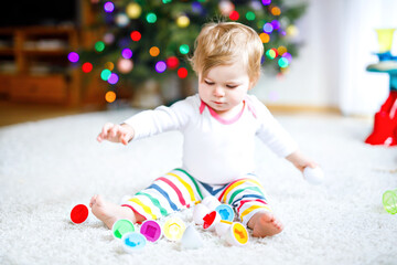 Fototapeta na wymiar Adorable cute beautiful little baby girl playing with educational toys at home or nursery. Happy healthy child having fun with colorful colorful shape sorter toy. Kid learning different skills,