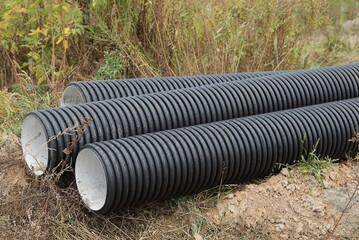three large black plastic sewer pipes lie on gray grass outside