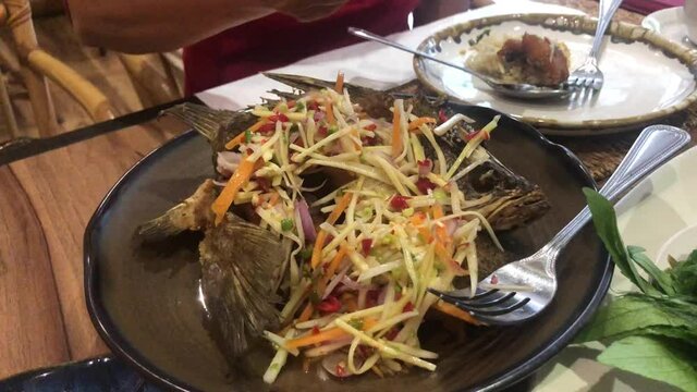 Deep fried seabass with sweet fish sauce eat with spice mango salad on wooden background.