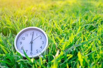 White alarm clock on grass background. Copy space.