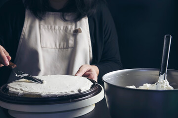Lady putting cream on baked cake making homemade bakery over black background