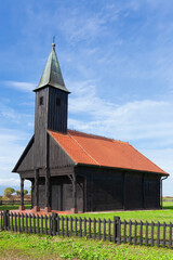 Black wooden church with small bell tower and black picket fence in front of it, with red tile roof