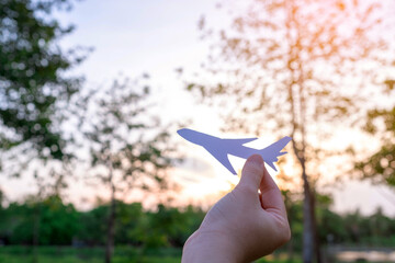 Hand of woman holding a paper cut of plane in nature at sunset. The pilot is that dream in the...