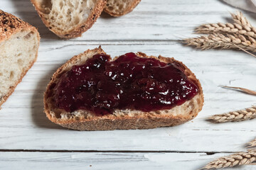 A slice of rustic bread smeared with jam on a white wooden board. Healthy food and farming concept