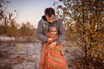 Family autumn walking. Cute girl with her father wrapping up in plaid among golden forest at fall
