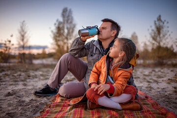 Fototapeta premium Family autumn walking. Cute girl with her father sitting on the plaid among golden forest at fall