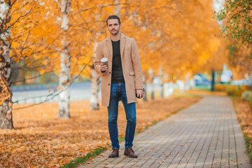 Fototapeta premium Young man drinking coffee in autumn park outdoors