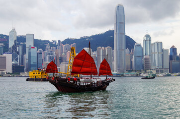 Traditional Chinese junk with red sails in Victoria Harbor, Hong Kong in China with panoramic city...
