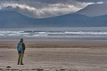 Person walking along a coastline in Ireland with rough sea. Rough sea at the Irish coastline. Person walking along Inch Beach in Ireland. Stormy sky above the irish coastline.