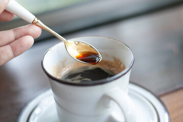 A hand holding siver spoon scooping some hot black coffee from a white ceramic mug