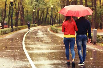 rain in the autumn park / young 25 years old couple man and woman walk under an umbrella in wet rainy weather, walk October lovers