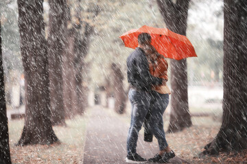 rain in the autumn park / young 25 years old couple man and woman walk under an umbrella in wet rainy weather, walk October lovers