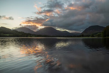 Beautiful sunrise landscape image looking across Loweswater in the Lake District towards Low Fell and Grasmere with vibrant sunrise sky breaking on the mountain peaks
