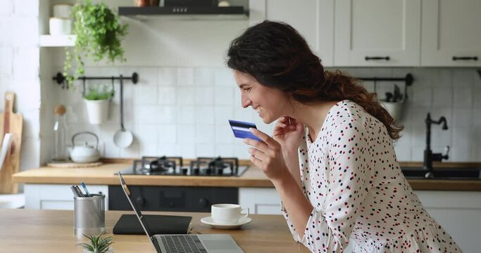 Housewife stands in domestic kitchen lean at dining table using laptop buy on internet by credit card. Good price great offer, enjoyment of e shopping, save money. Easy distant e-pay from home concept