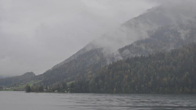 Time-lapse shot of heavy autumn rain, fog and clouds formation, turbulent cloudy sky over Aegeri lake and Rossberg mountain covered with coloured virgin H&ouml;lliwald forest, Pre-Alps, Central Switzerland