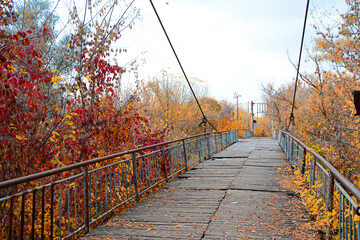 View of the old wooden bridge over the river in the park on a autumn day.