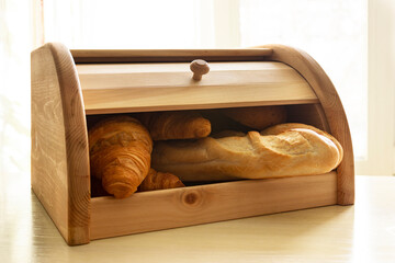 Wooden bread box full of different bakery on the bright sunlight background. Fresh baguette and croissants in the breadbox. - obrazy, fototapety, plakaty