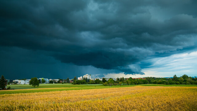Germany, Stuttgart, Dramatic dark sky of a heavy storm front and thunderstorm above village and fields in summer