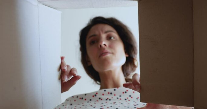 Close up inside of carton box bottom view, female open parcel looks at broken items feels angry. Complaint of client, refund bad-quality goods, negative experience buying on internet webstores concept