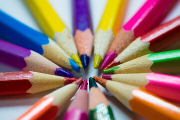 Colored and sharpened pencils lie in a circle next to each other on a white background close-up.