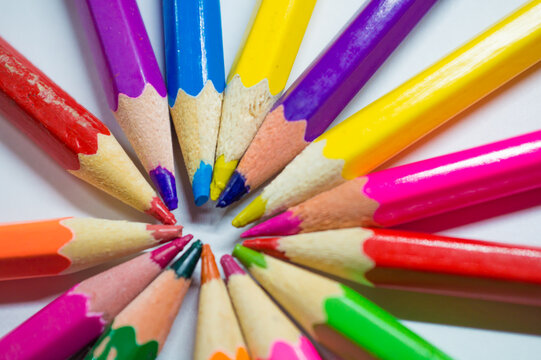 Colored and sharpened pencils lie in a circle next to each other on a white background close-up.
