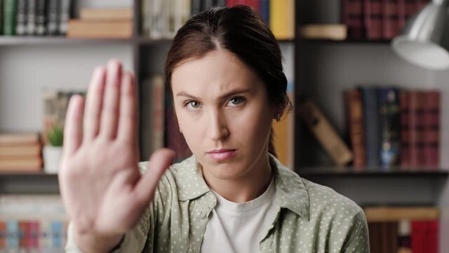 Woman palm STOP. Frowning serious woman in office or room in apartment looking at camera raises her hand and shows her palm signaling STOP
