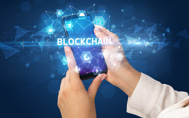 Female hand holding smartphone with BLOCKCHAIN inscription, modern technology concept