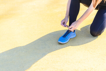 young female athlete tying blue sports shoes and projecting shadow on yellow floor