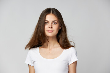 Obraz premium A beautiful brunette girl with long hair in a white T-shirt looks forward 