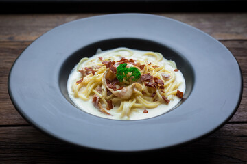 Spaghetti carbonara with a white sauce and on top with crispy bacon and parsley.