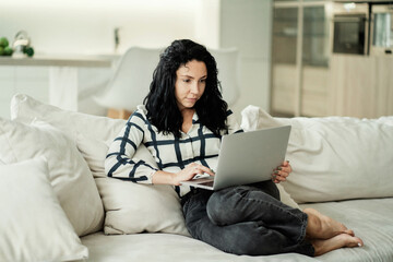 Fototapeta premium a young woman of European appearance ethnic, sitting on the couch holding a laptop computer and doing work at home online. modern residential design apartment