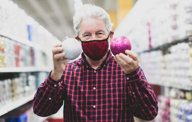 A senior white haired man holding two glittery christmas balls, silver and purple, wearing a...