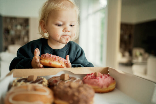 The Most Delicious Dessert Baking Doughnuts From The Bakery, With An Appetite Eats Baby Girl Kids On Their Holiday. Courier Fast Delivery Of Food Sweets To Your Home