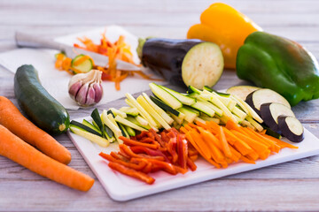 Fresh vegetables on a wooden table with a mix of sliced carrots, zucchini, eggplant and peppers ready to be cooked - healthy eating vegetarian or vegan concept