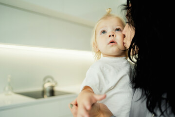 Fototapeta premium time together portrait of a little interesting girl blonde baby kids and a cheerful young kind mother brunette, hugging show a warm attitude to each other. young family