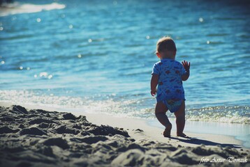 dziecko spacerujące w słoneczny dzień po piaskach plaży na brzegu morza - obrazy, fototapety, plakaty