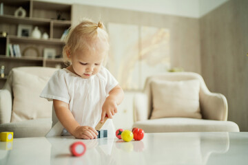 Naklejka premium cozy home apartment, a 3-year-old girl plays children's topical games. Blonde Caucasian appearance. Banner for advertising
