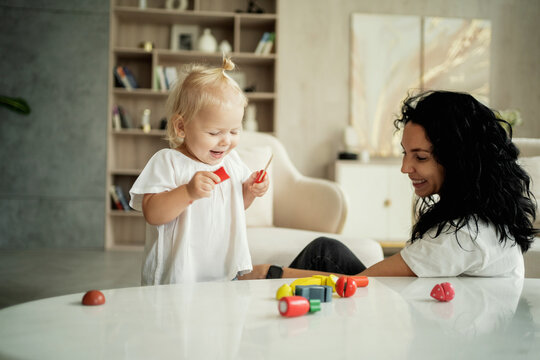 little cute blonde girl of European appearance baby and nanny brunette play with children's toys in the living room. cozy day in the apartment with the whole family.