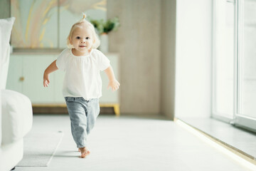 Fototapeta premium portrait of a girl child kids running around playing in the apartment, dressed in a white shirt and blue jeans. white apartment design, daylight in the window