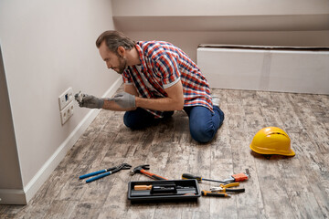 Young caucasian electrician putting power socket into wall