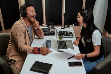 Portait of two cheerful radio hosts, young man and woman laughing while discussing various topics,...