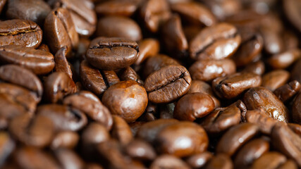 Full frame shot of roasted coffee beans in detail. Group of black aromatic seeds in close up with copy space. Background from a heap of dark fresh grain.