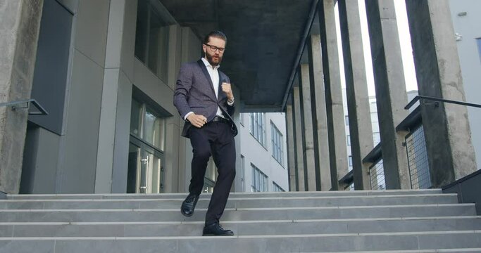 Close up of likable cheerful satisfied adult businessman funnily dancing while going down the stairs from modern office building