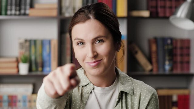 Woman beckoning finger gesture. Happy positive smiling woman in office or apartment looks at camera and points with finger and invite gesture asks to come to her