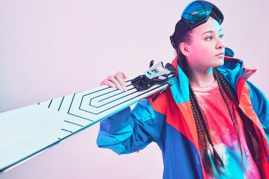 Sporty young asian female skier in stylish colorful winter sportswear with ski posing in studio in neon light