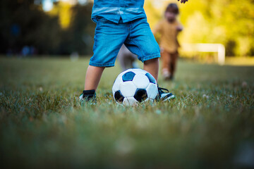Fototapeta na wymiar Legs of little boy playing football on grass.