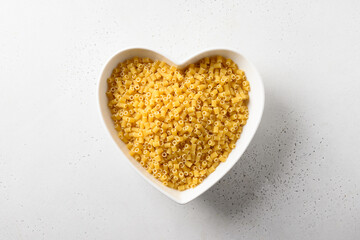 Raw ditalini pasta in white plate in shape of heart on white background. Top view.